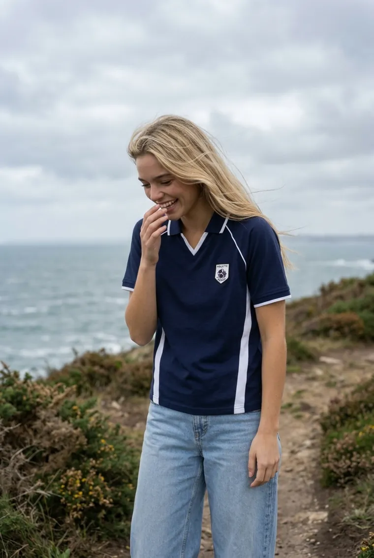 Jeune femme en polo Rospeli bleu marine, riant sur un chemin côtier